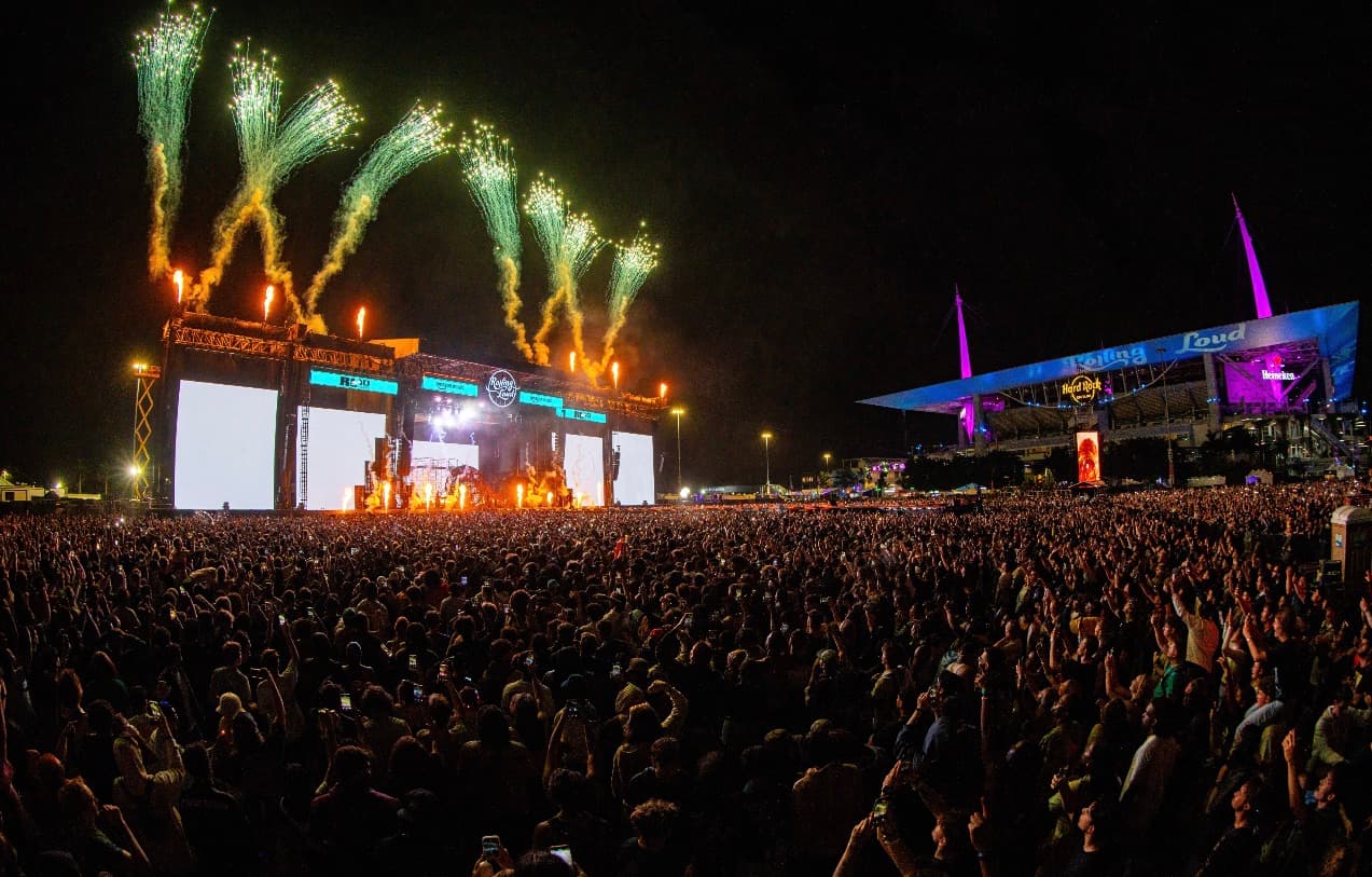 Large outdoor concert crowd with stage lights and fireworks